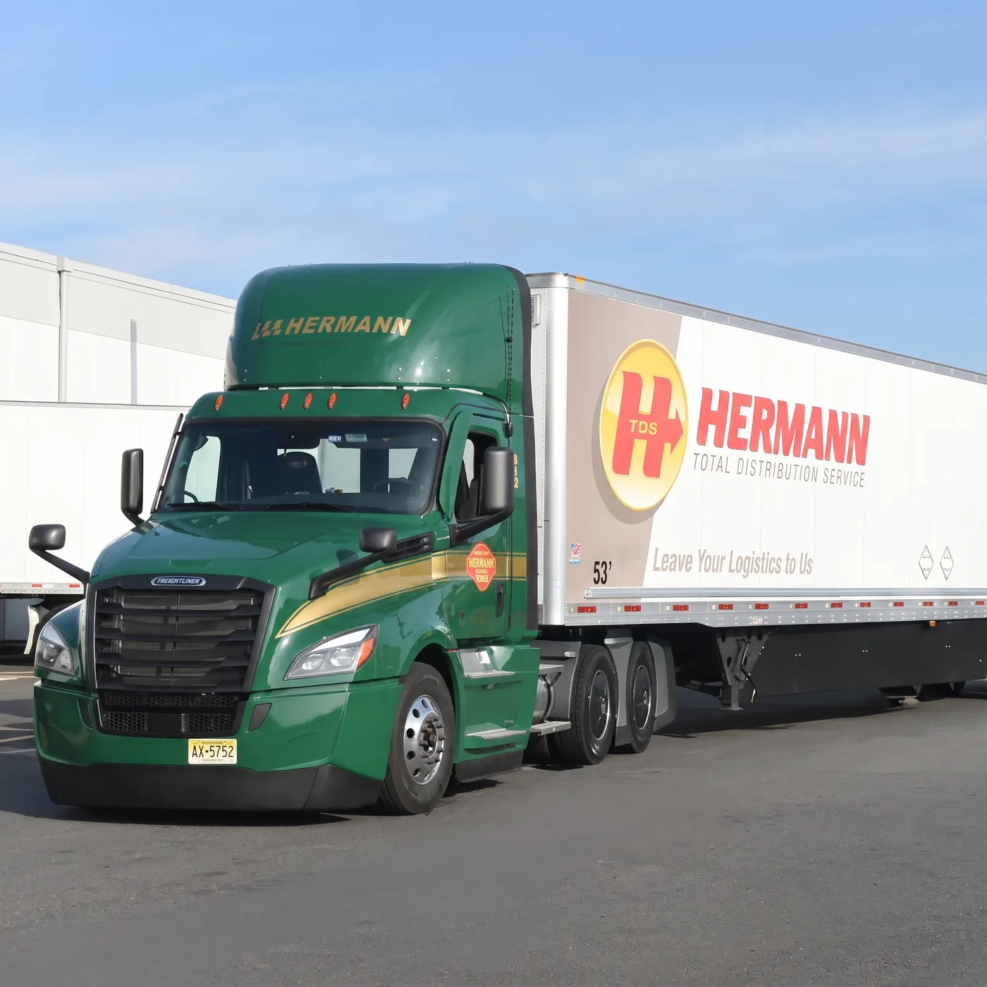A green Hermann Freightliner tractor with a 53-foot Hermann Total Distribution Service trailer
