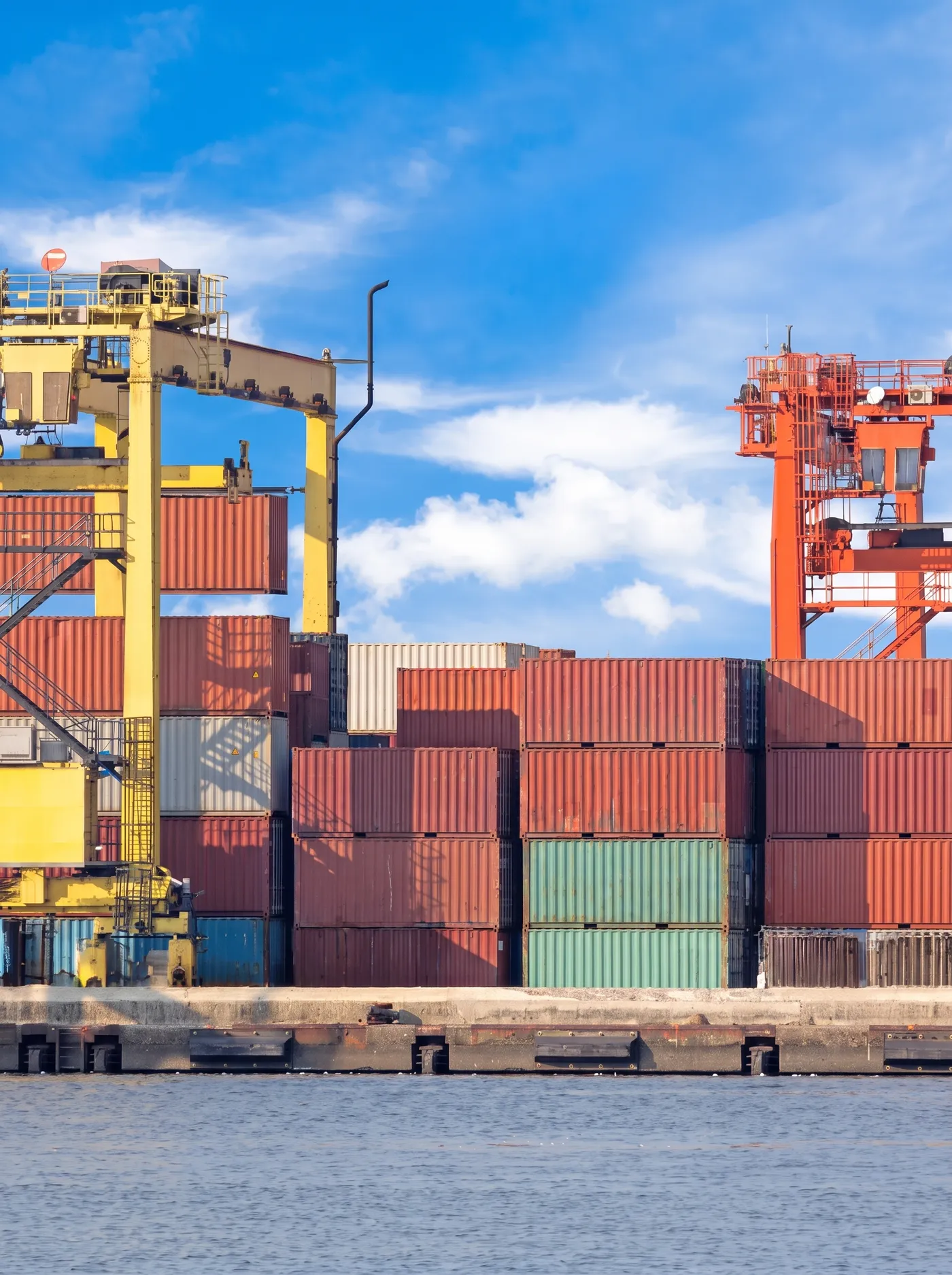 Shipping containers stacked under gantry cranes at the port